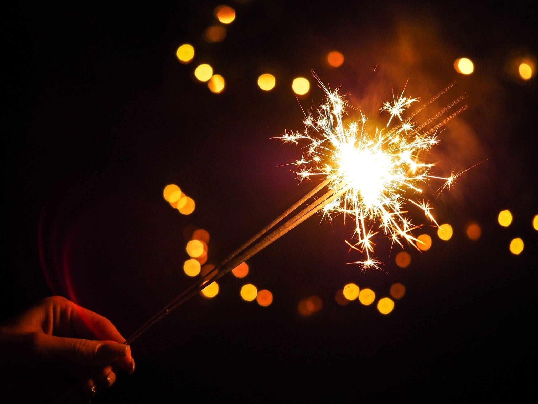 Hand holding lit sparkler at night